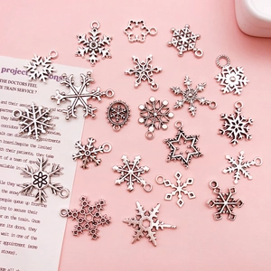 Detailed view of silver snowflake charms for DIY jewelry making on a pink background