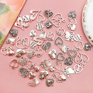 Variety of heart-shaped alloy charms for DIY jewelry making on a pink background