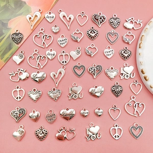 Collection of various vintage alloy heart pendants for DIY jewelry making on pink background