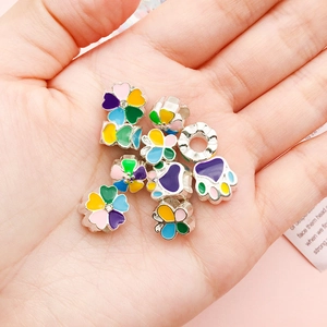 Detail of colorful enamel charms for DIY bracelets held in palm showing scale