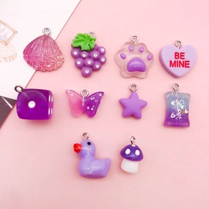 Close-up of assorted purple resin charms including shells, grape, and cat paw for DIY jewelry