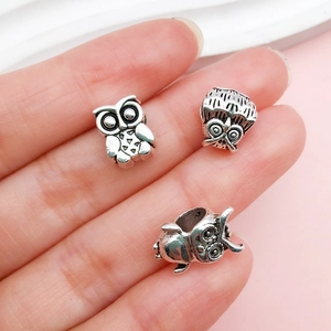Macro detail of antique silver owl charms for DIY bracelets shown on a fingertip