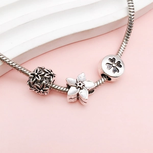 Detailed macro view of silver alloy snake chain bracelet with floral charms on pink background