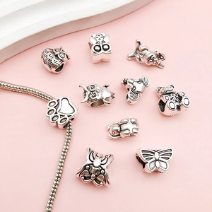 Macro shot of silver owl and elephant charms with a snake chain on a pink base