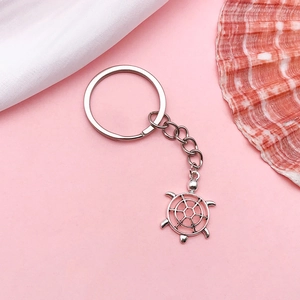 Silver turtle and helm charms on keychains with seashells and a pink backdrop