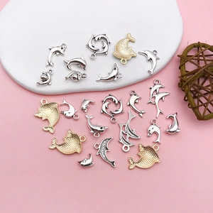 Macro shot of silver and gold dolphin charms on a pink aesthetic display for DIY jewelry