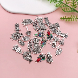Flat lay of vintage silver owl charms for DIY jewelry on a soft pink background