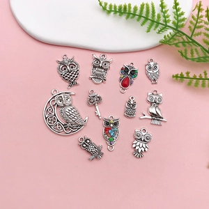 Flat lay of antique silver owl charms for DIY jewelry making on pink background