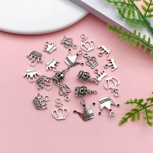 Detailed flat lay of silver crown pendants for DIY jewelry on a pink background