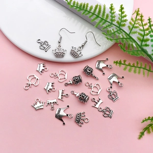 Macro detail of antique silver crown charms and princess earrings on pink backdrop