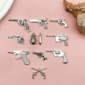 Detailed view of silver antique gun and bullet charms for DIY jewelry making on pink background