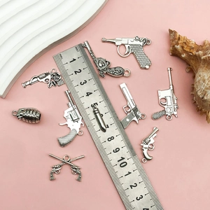 Vintage silver alloy gun and bullet charms for DIY jewelry making on pink background