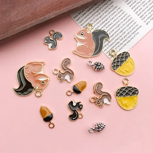 Detailed flat lay of squirrel and acorn charms for DIY jewelry on pink background