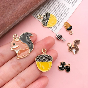 Close-up of squirrel and acorn alloy charms held by hand to show size for DIY jewelry