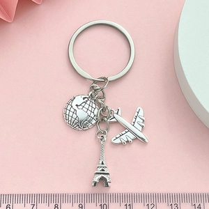 Silver travel keychain with Eiffel Tower, globe, and plane charms on pink card background