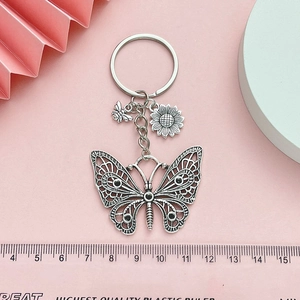 Minimalist silver butterfly keychain with sunflower and bee charms on pink background