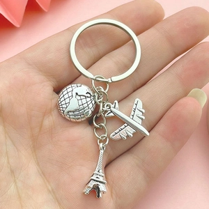 Silver Eiffel Tower, globe, and airplane travel keychain held against a pink background