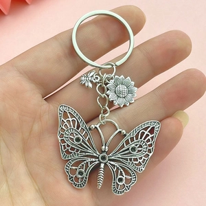 Vintage silver butterfly keychain with sunflower and bee charms held against a pink backdrop