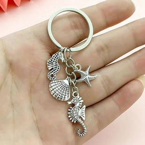 Marine keychain featuring silver seahorse, starfish and shell charms held by hand