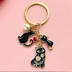 Détail d'un porte-clés doré avec trois chats en émail noir et un pendentif perle