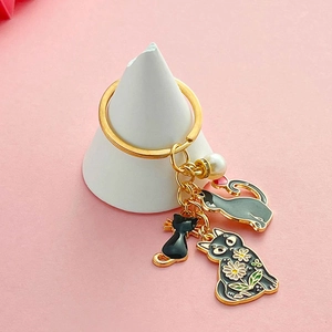 Porte-clés chat noir mignon avec trois pendentifs et perle sur fond rose pastel