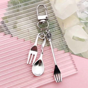Detailed view of silver alloy miniature cutlery charms with fork and spoon on pink surface