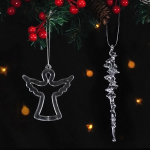 Clear crystal angel and icicle Christmas ornaments hanging on a pine tree with warm bokeh