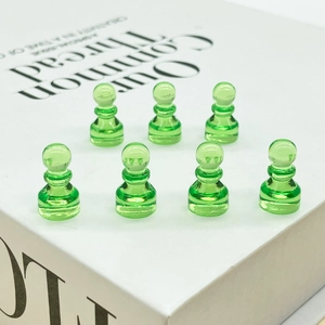 Translucent green crystal chess pieces for board games arranged on a white book surface