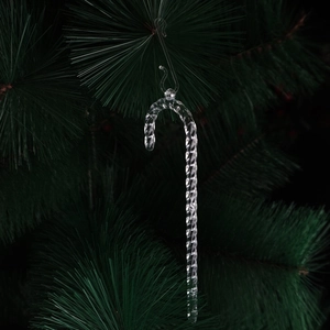 Detail of transparent candy cane ornament with spiral texture hanging on a green tree