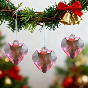 Three pink faceted heart crystal ornaments hanging on a Christmas wreath with gold bells