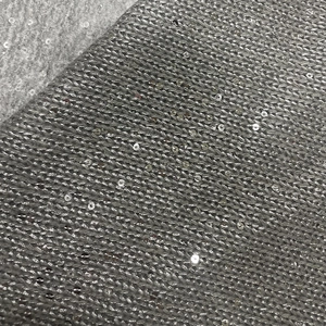 Macro view of grey knit fabric with dense silver sequins and intricate woven texture