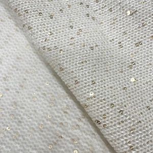Macro shot of white knitted fabric featuring gold sequins and soft wool texture detail