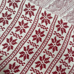 Macro detail of red and white Nordic snowflake pattern on knitted wool fabric texture
