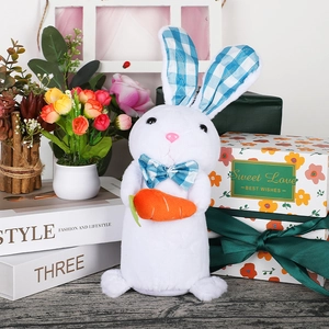 Close-up of white plush bunny with blue plaid ears holding a carrot on a table