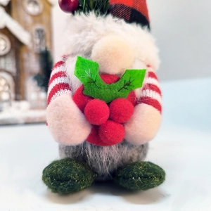 Gnome de Noël avec bonnet à carreaux tenant des baies rouges et du houx en gros plan