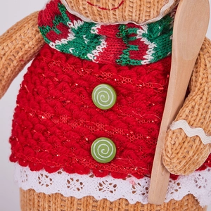 Detail of knitted gingerbread doll with red dress, green buttons, and a wooden spoon