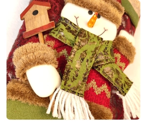 Detail of plush Christmas snowman ornament with fleece hat and small wooden birdhouse