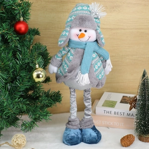Retractable snowman Christmas doll in blue knit sweater standing by an indoor holiday tree