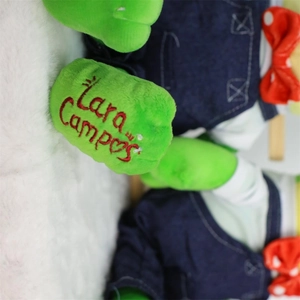 Green plush frog toy with denim overalls and custom embroidery detail on the hand