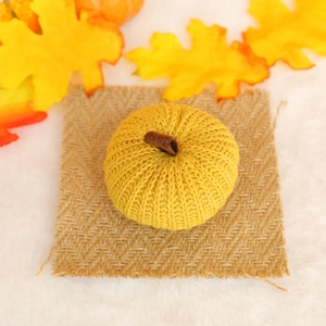 Detail of knitted orange pumpkin decoration with brown stem on rustic burlap and maple leaves