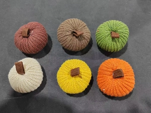 Close-up of six assorted knitted pumpkins for harvest festival decor on dark fabric