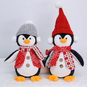 Pair of plush Christmas penguin figurines with knitted hats and striped scarves on snow