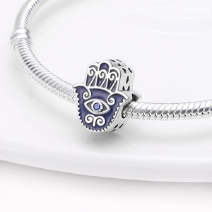 Macro-opname van een zilveren Hamsa-bedel met blauw emaille en kristal op een armband
