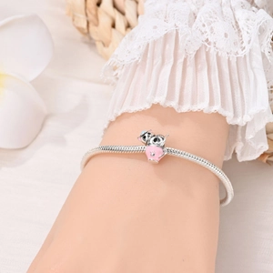 Detail van zilveren slangenarmband met roze emaille kattenbedel en bloemige achtergrond