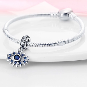 Macro-opname van zilveren slangenarmband met boze oog hanger en blauwe kristallen