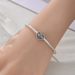 Silver bracelet detail showing a heart charm with orange flowers on a model's wrist