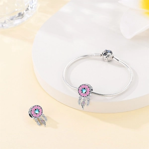 Macro detail of silver dreamcatcher charm with pink enamel and blue heart gem on snake chain