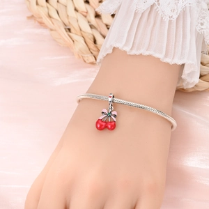 Close-up of red cherry charm bracelet with pink bow on silver snake chain for women