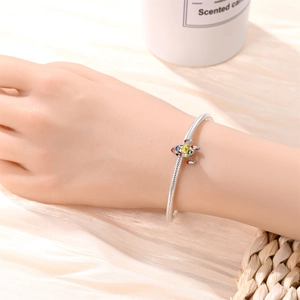 Close-up of a silver snake chain bracelet with a colorful enamel airplane charm on a wrist