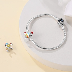 Detail of silver snake chain bracelet with yellow enamel rocket charms and starry blue zircons